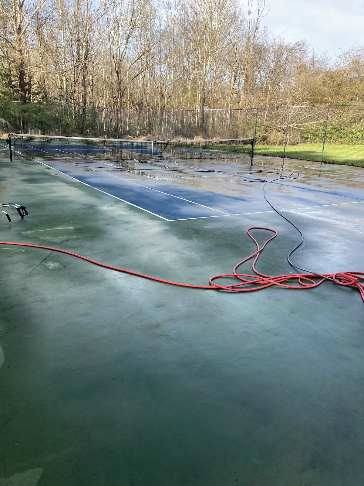 Tennis court being pressure washed with red hoses laid out